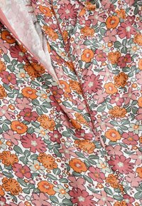 Tkanina w kwiaty z dużymi pomarańczowymi, różowymi i kremowymi kwiatami na białym tle z zielonymi liśćmi; zawiera ukryty zamek.