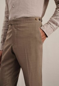 Pantalons taillés marron clair avec une texture lisse, dotés d'une coupe droite, de deux boutons à la taille et de poches latérales.