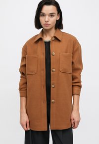 Vaaleanruskea napillinen takki, jossa on kaulus, kaksi etutaskua ja käännetyt hihat, valmistettu lämpimästä, teksturoidusta materiaalista.