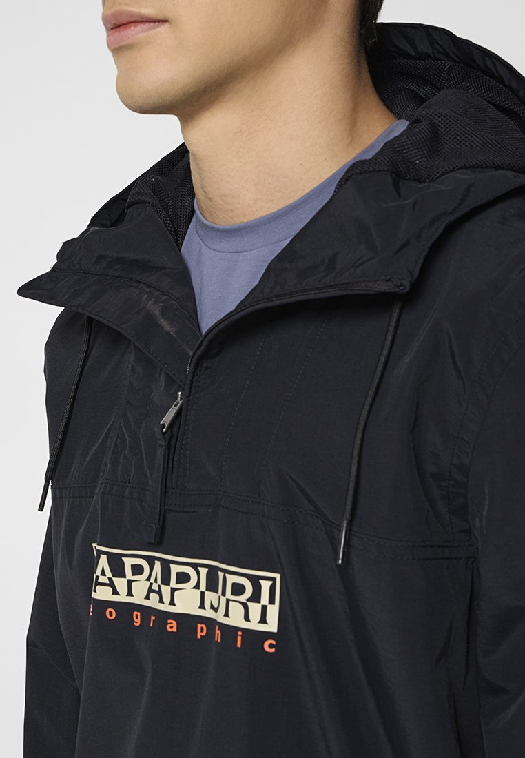 Man in zwarte hoodie met rits en Napapijri-logo over een blauwe t-shirt met ronde hals, die naar links kijkt, afgesneden op kin en schouders.