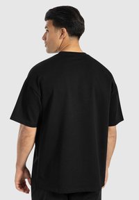 Schwarzes Baumwoll-T-Shirt mit lockerem Schnitt, kurzen Ärmeln und Rundhalsausschnitt, das eine glatte Textur und ein minimalistisches Design aufweist.