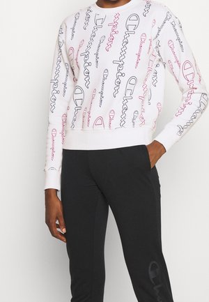 Vit sweatshirt med färgglad "Champion"-logotyp i rosa och mörkblått, med långa ärmar, ribbade muddar och en kort design. Matchas med svarta byxor.