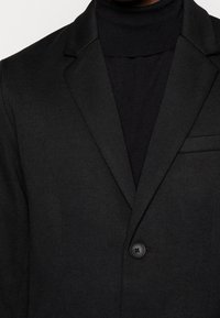 Blazer nero realizzato in un tessuto testurizzato con chiusura a un bottone, rever a punta e tasca sul petto.