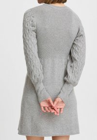 Abito grigio in maglione con corpetto a coste e maniche in maglia a trecce testurizzate. L'orlo è leggermente svasato con una finitura liscia.