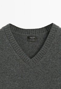 Donkergrijze kasjmieren trui met V-hals, ribgebreide kraag en manchetten, met een zachte textuur. Etiket leest "Massimo Dutti, 100% kasjmier."