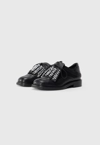 Black shoes with a textured, reptile-like material, featuring a wide strap adorned with large, shiny rhinestones and a flat sole.