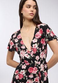 Abito floreale in tessuto nero con maniche corte, scollatura a V profonda e vita elastica arricciata. Fiori prevalentemente rosa e bianchi.