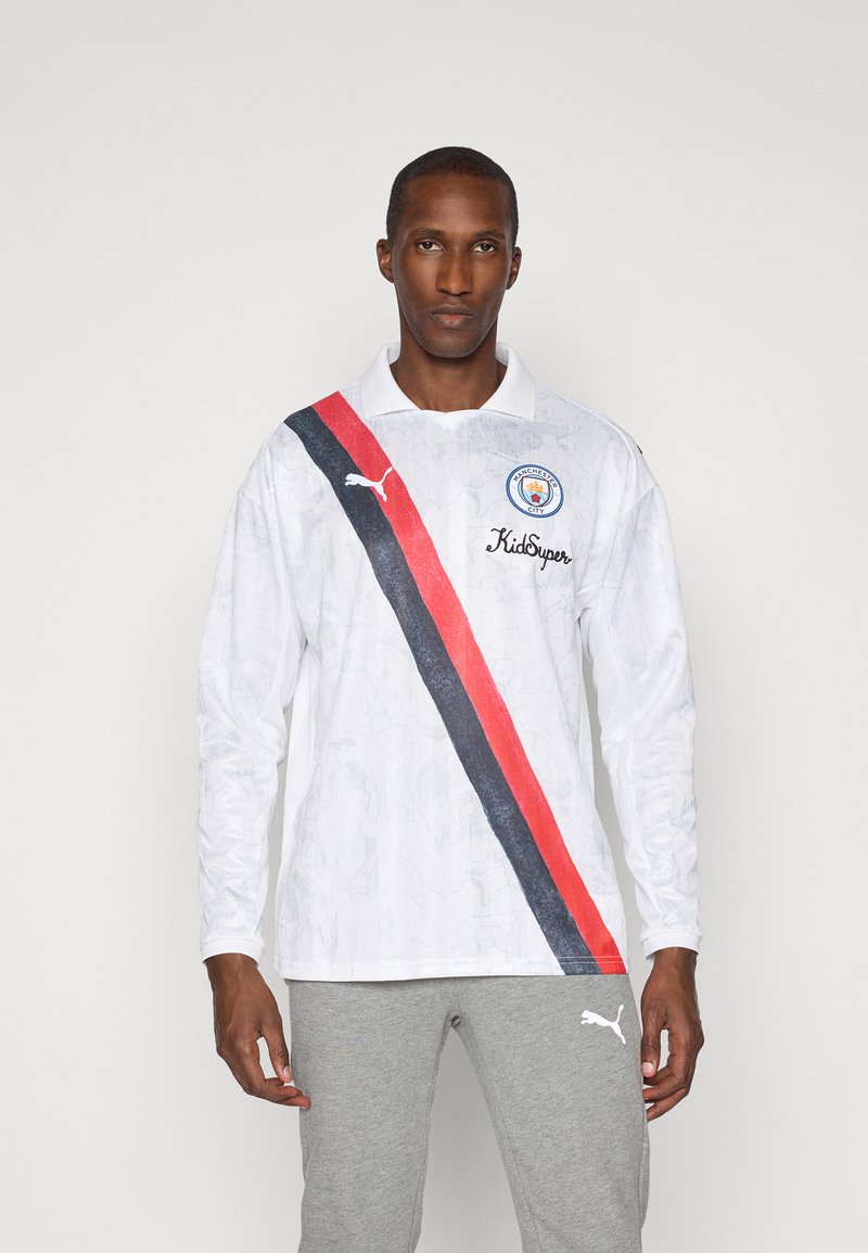 Hosszú ujjú fehér póló, texturált mintával, átlós piros és fekete csíkkal, Manchester City márkázással.