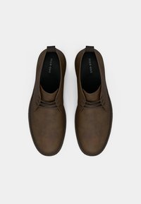 Rudos odinės bateliai su lygiu paviršiumi, apvalia nosimi ir dviem raišteliais, pasižyminčiais subtiliu toniniu siuvimu aplink kraštus.