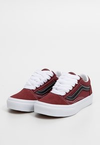 Pár nízkých vínově červených semišových tenisek s bílými silnými šňůrkami, černým bočním proužkem, bílým prošíváním a bílými gumovými podešvemi na jednobarevném pozadí.