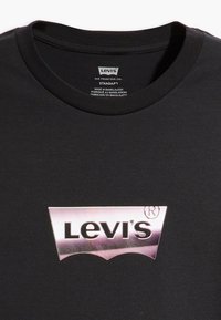 Černé bavlněné tričko s metalickým stříbrným logem Levi's v klasickém obloukovém designu. Klasický kulatý výstřih se žebrovanou texturou. Podrobnosti o štítku viditelné uvnitř.