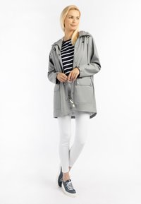 Ljusgrå vattentät jacka med huva, silverfärgade detaljer och framfickor, bärs över en randig topp och paras med vita leggings och blå skor.