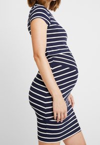 Sukienka ciążowa w kolorze granatowym z białymi poziomymi paskami. Krótkie rękawy i dopasowany fason podkreślający brzuszek. Miękka, elastyczna tkanina.