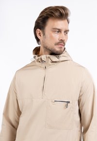 Beige lichtgewicht jas met een capuchon, halve rits aan de voorkant en een ritszak op de linkerborst. Soepele textuur en minimalistisch ontwerp.