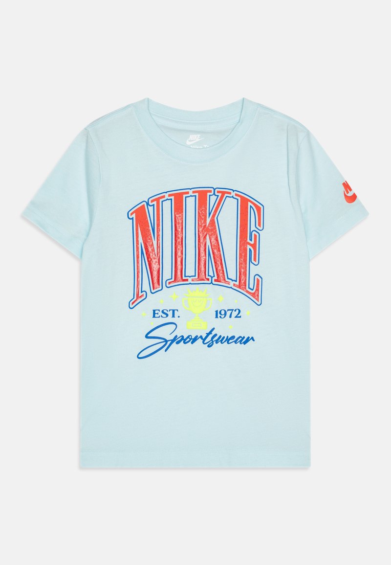 Svijetloplava pamučna majica s velikim crvenim i plavim "NIKE" logotipom, grafikom trofeja i tekstom "Sportswear" u kurzivu. Kratki rukavi.