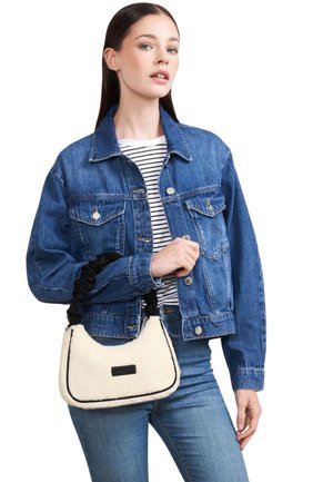 Femme portant une veste en jean bleue et un jean, tenant un petit sac à main en sherpa blanc avec une poignée noire tressée.