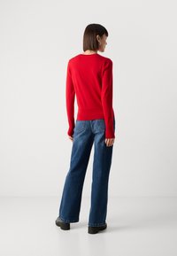Red knit sweater with long sleeves, ribbed hem, paired with wide-leg blue denim jeans and black platform shoes. Rear view of the outfit.