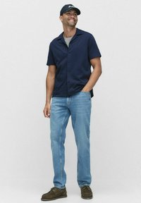 Marine gestreept T-shirt met korte mouwen, grijs T-shirt met ronde hals eronder, lichtblauwe spijkerbroek, bruine suède schoenen, zwarte honkbalpet.