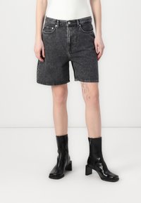 Shorts en denim noir avec un design à jambes droites, dotés de poches et d'ourlets effilochés. Assortis à des bottines noires brillantes.