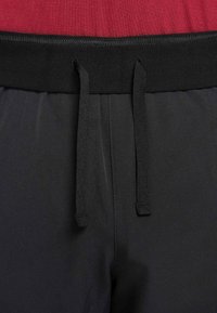 Calções atléticos pretos com cós elástico e cordão. Textura lisa com tecido vermelho contrastante na parte superior.