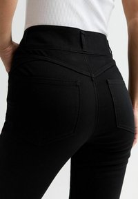 Jean noir taille haute en denim, avec une texture lisse, des poches arrière et une silhouette ajustée.