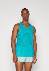 Débardeur de sport turquoise avec un motif découpé géométrique, fabriqué en tissu léger ; associé à un short bleu clair.