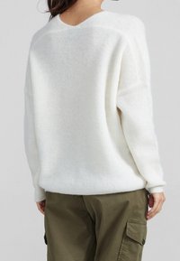 Pull blanc surdimensionné en fil duveteux avec une texture douce. Doté d'une encolure large et de coutures d'épaules tombantes. Associé à un pantalon cargo olive.