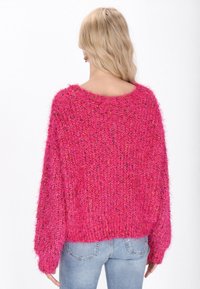 Roze donzige trui met een losse pasvorm, gestructureerd breipatroon, wijde halslijn en lange mouwen, gecombineerd met lichtblauwe jeans.