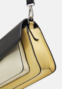Dreilagige Handtasche aus schwarzem, cremefarbenem und gelbem Leder. Sie verfügt über eine glatte Textur, kontrastierende Nähte und einen Metallclip zur Befestigung.
