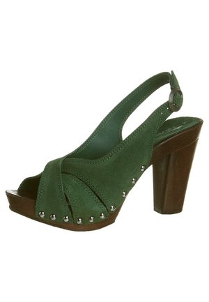Sandale en suède verte avec un design à talon ouvert, un talon en bois épais, et des clous en argent décoratifs à l'avant. orteil ouvert avec des sangles croisées.