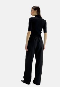 Zwarte korte mouwen top gecombineerd met losse, hoge zwarte broeken. De outfit heeft een gladde stof en een elastische tailleband.
