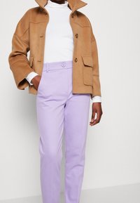 Bruine wollen blend jas met een hoge kraag, twee voorzakken en een knoopsluiting, gecombineerd met lavendelkleurige op maat gemaakte broek.