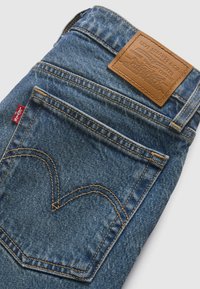 Δερμάτινα τζιν με ξεθωριασμένο μπλε χρώμα. Διαθέτουν καφέ δερμάτινη ετικέτα, ραμμένες τσέπες και κίτρινη ραφή. Μικρό κόκκινο λογότυπο κοντά στην τσέπη.