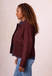 Burgundy suede jacket with a collar, snap buttons, and a front pocket, paired with a blue denim shirt and light blue jeans.