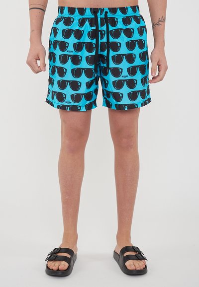 Pantaloni da nuoto di un vivace colore turchese con un motivo di occhiali da sole neri. Vita elastica con cordino, realizzati in tessuto leggero.
