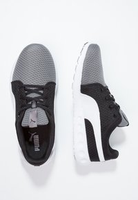 Baskets de sport noires et grises avec une tige en mesh, un bout rond, des accents blancs et une semelle texturée avec des détails de traction circulaires.