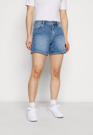 Pantalones cortos de mezclilla en azul claro, con un diseño clásico de cinco bolsillos, corte recto y dobladillos enrollados. Combinados con zapatillas blancas.