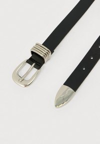 Melns ādas jostas siksna ar sudraba sprādzīti, rakstaina josla un smaili veidots gals. Iekļautas caurumi regulējamam izmēram.