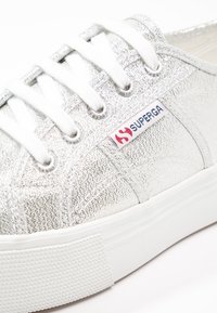 Baskets Superga argentées texturées avec lacets blancs et semelle en caoutchouc, affichant le logo de la marque sur une étiquette en tissu près des œillets.
