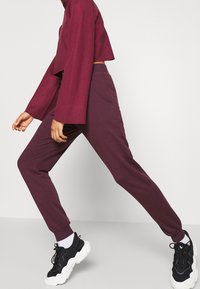 Top corto burdeos con mangas anchas combinado con pantalones con pinzas a juego. La modelo lleva zapatillas negras con suelas blancas. Textura de tela suave.