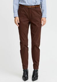 Braune Baumwollhosen mit schmaler Passform, ausgestattet mit einem flachen Bund, Gürtelschlaufen und einem Reißverschluss. Kombiniert mit schwarzen spitzen Stiefeletten.