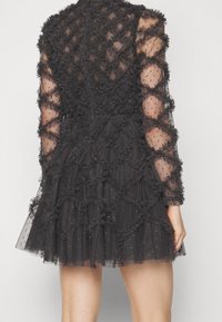 Une robe noire avec une couche texturée de volants et de tissu transparent. Manches longues avec des motifs d'étoiles, jupe évasée et col haut.