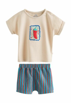 Bézs színű rövid ujjú kisgyermek póló, chilipaprika folttal, rajta az „Chillin' Out” felirat, kék, piros és barna csíkos rövidnadrággal párosítva.