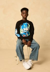 Mustaga pikka varrukaga särk, millel on värvilised graafilised kujundid, sisaldades tegelasi, koos helesiniste lõdva lõikega teksade ja valgete tossudega.