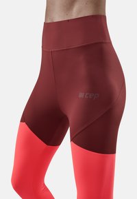 Leggings de sport bordeaux et rose avec un design en color-block. Texture lisse, taille haute et logo subtil sur le côté.