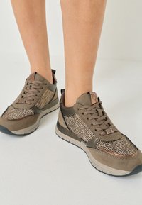 Des chaussures de sport marron avec une tige en tissu tissé, des accents en daim et une semelle rembourrée avec des motifs de semelle distinctifs.