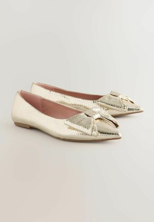 Scarpe flat con punta affilata, realizzate in materiale metallic oro testurizzato. Presentano un fiocco decorativo sulla parte anteriore e un interno rosa chiaro.