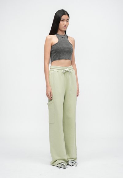 Sivý rebrovaný crop top a mäkké, svetlozelené nohavice s širokými nohavicami, elastickým pásom a bočnou vreckom. Metalické špicaté podpätky dotvárajú celkový vzhľad.