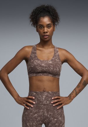 Sport-bh med brun sprøjtetryk, tykke stropper og bred kant, kombineret med højtaljede matchende leggings med et lignende mønster.