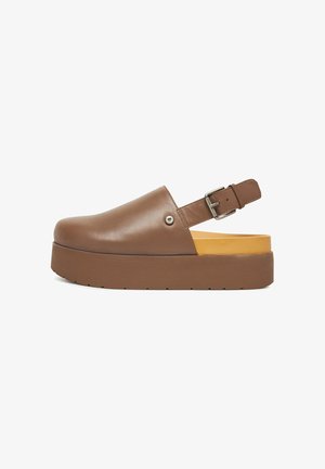 Zuecos de plataforma de cuero marrón con punta redondeada, correa trasera con hebilla y suela de goma texturizada. El interior cuenta con un acolchado de acento naranja.